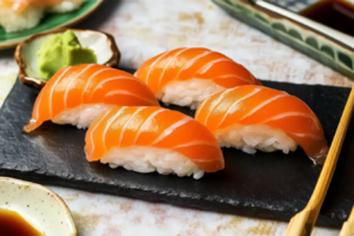 Four pieces of sushi order topped with fresh salmon, served with wasabi on a slate plate, showcasing their vibrant color and traditional Japanese presentation.