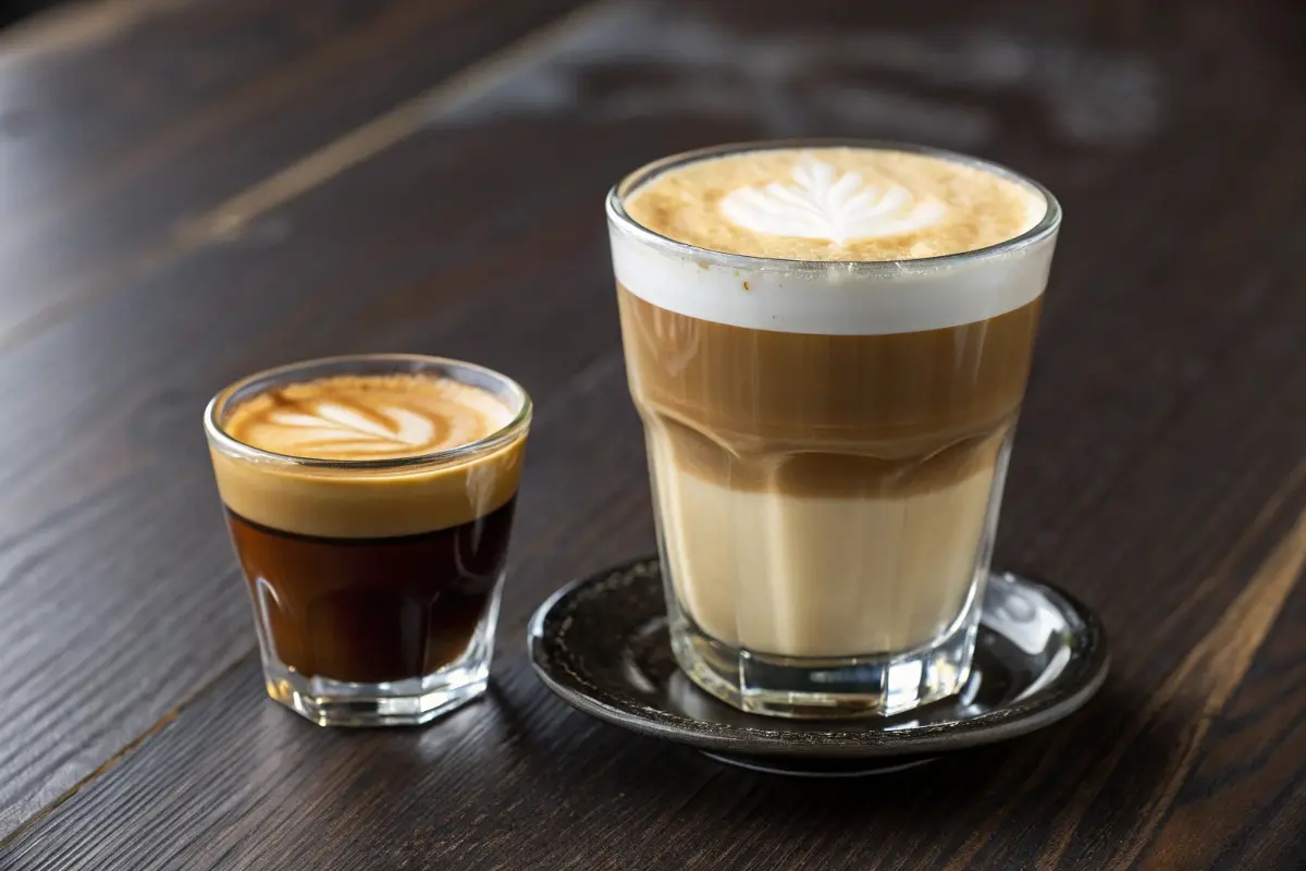 A cortado and a macchiato served side by side in clear glasses, highlighting their differences in milk-to-espresso ratios and presentation.